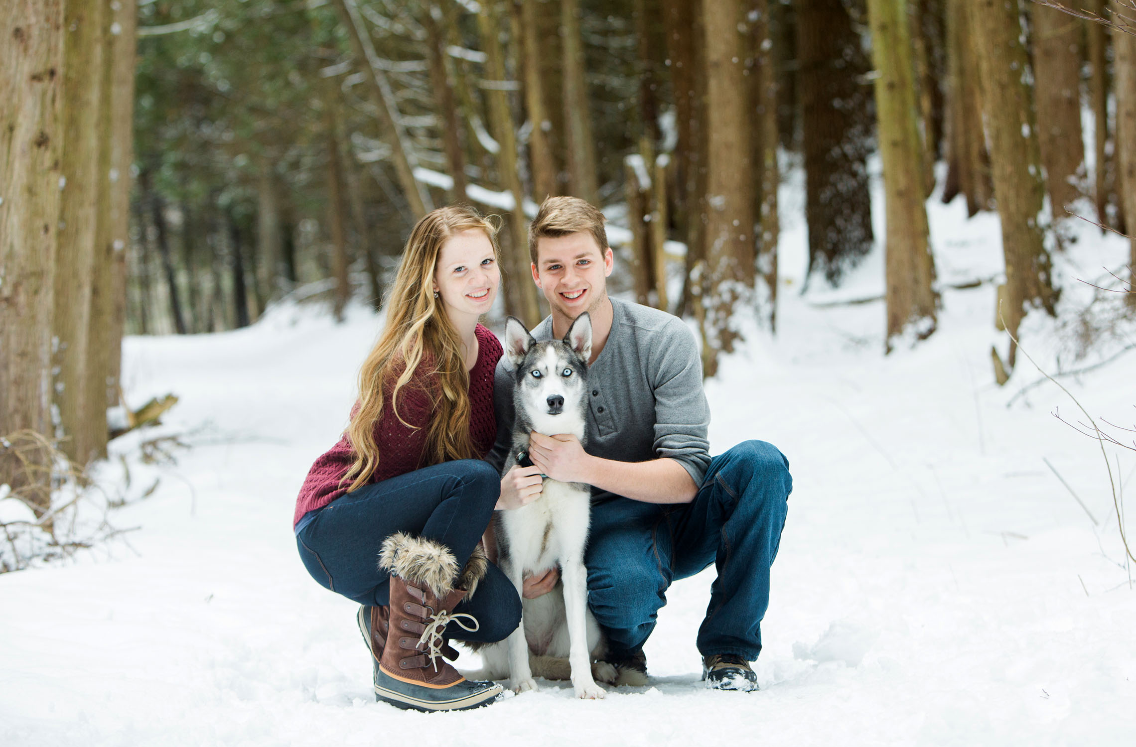 Young couple with husky puppy in the forest with snow on the ground. 