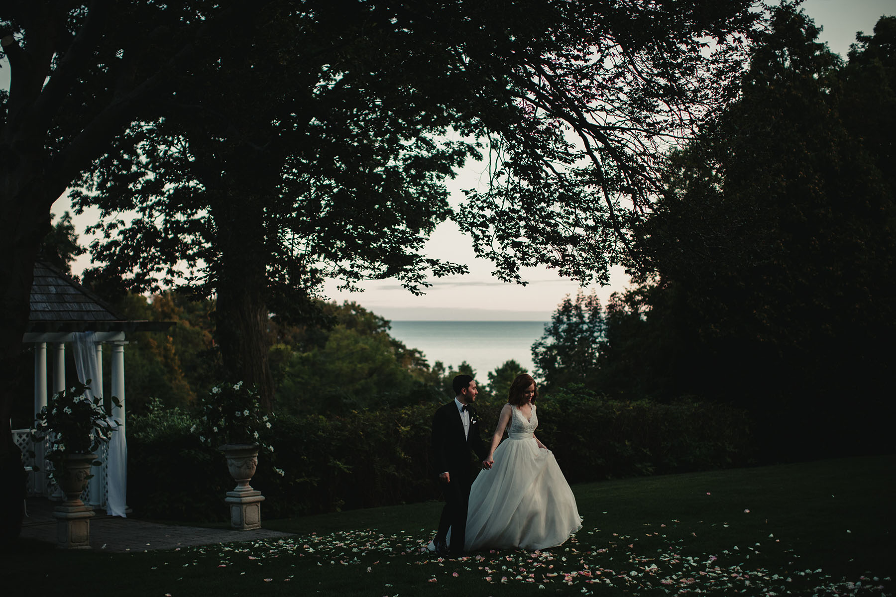 Beautiful setting of golf course over looking Lake Ontario. Bride and groom walking thru the grass.