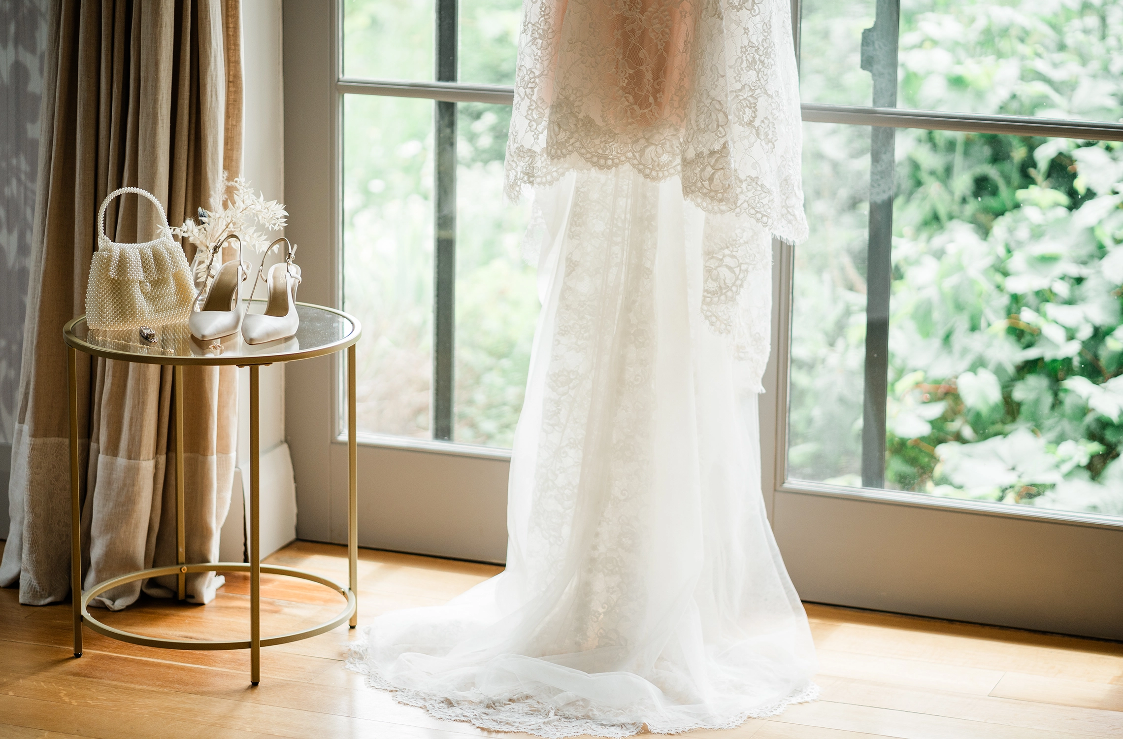 Wedding dress hanging by French doors at Compass Rose Suites — lace and long train.